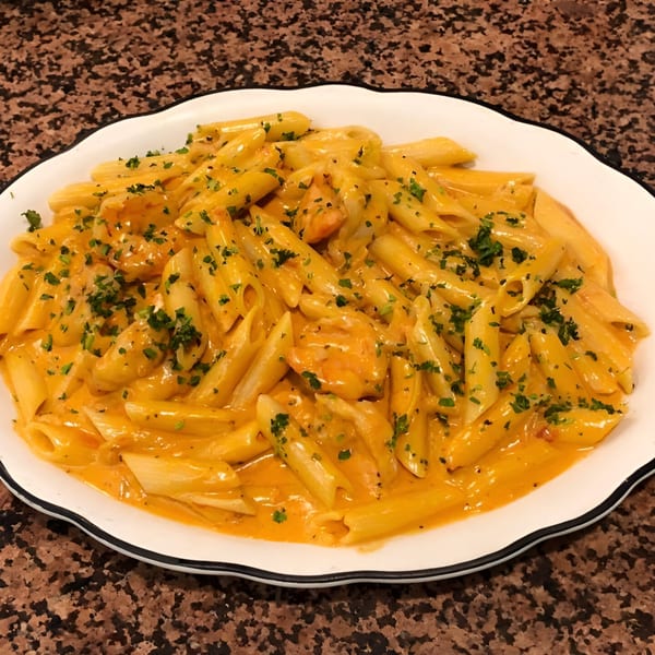 Penne pasta with creamy orange sauce and chopped parsley in a white scalloped dish.