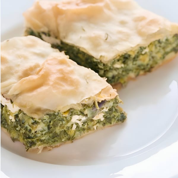 Two slices of spinach and feta pie, known as spanakopita, on a white plate.