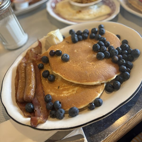 Diner breakfast plate with blueberry pancakes, bacon, sausage, and butter.
