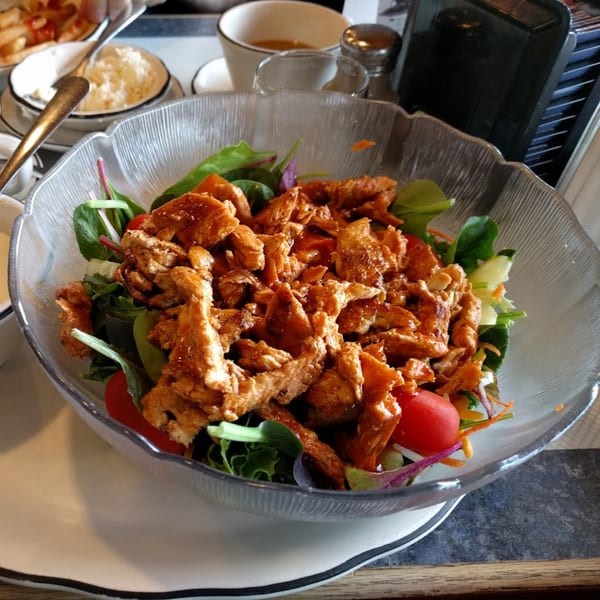 A large glass bowl of Galaxy Diner's chicken salad with mixed greens, tomatoes, and dressing.