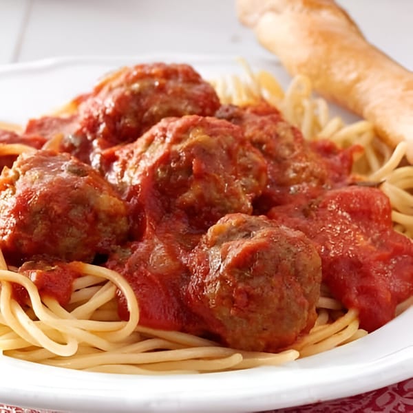Spaghetti and meatballs with red sauce, served with a breadstick on a white plate.