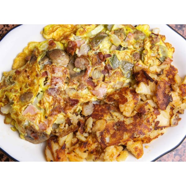 A diner-style omelet with mushrooms, peppers, and ham, served with crispy home fries.